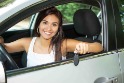 Young woman sitting in a car holding keys out the window.